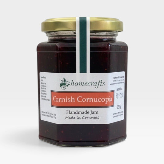 A glass jar of Homecrafts Cornish Cornucopia Handmade Jam with a gold lid and white label, set against a plain light gray background.