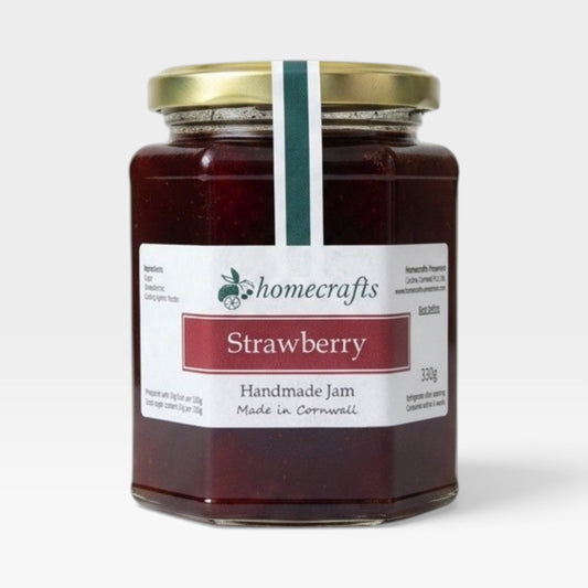 A glass jar of Homecrafts Strawberry Handmade Jam with a gold lid and white label, set against a plain light gray background.